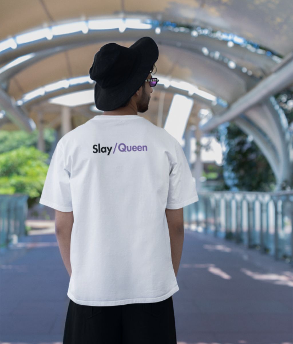 A man shows off his white shirt featuring the phrase "slay / queen" radiating positivity and style.