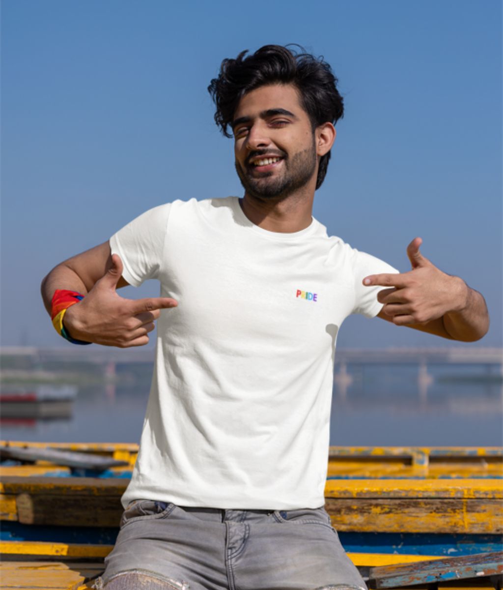 A man proudly wears a white t-shirt featuring the word &quot;pride&quot; printed in bold colourful letters.
